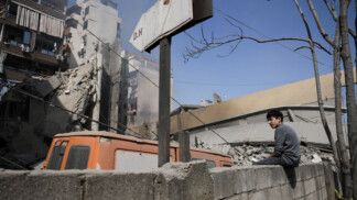 Garoto senta no muro diante de prédio destruído por ataques israelenses