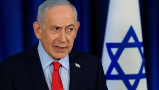 O primeiro-ministro Benjamin Netanyahu olha para o lado, à frente da bandeira de Israel