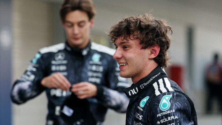 Kimi Antonelli sorri em primeiro plano enquanto George Russell aparece ao fundo