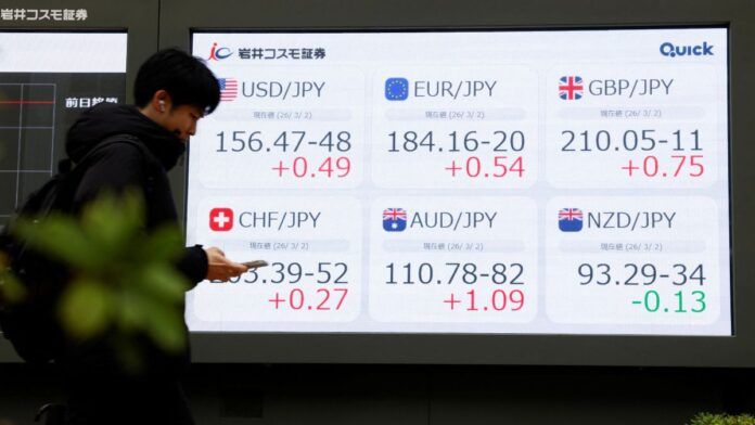 Pessoa olha o celular diante de painel com números do mercado de ações