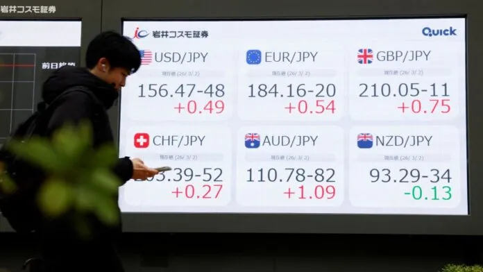 Pessoa olha o celular diante de painel com números do mercado de ações