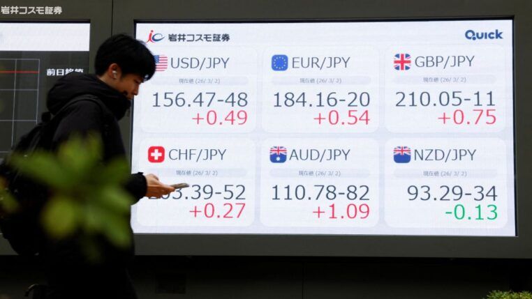 Pessoa olha o celular diante de painel com números do mercado de ações