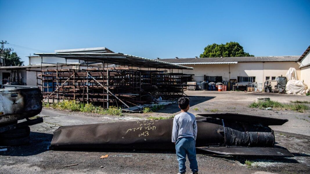 Um menino observa os destroços de um míssil iraniano que caiu em um kibutz, após o Irã lançar ataques com mísseis em resposta aos ataques dos EUA e de Israel.