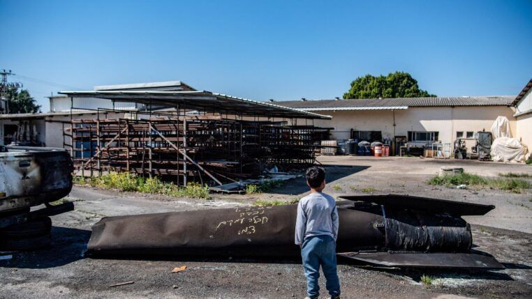 Um menino observa os destroços de um míssil iraniano que caiu em um kibutz, após o Irã lançar ataques com mísseis em resposta aos ataques dos EUA e de Israel.