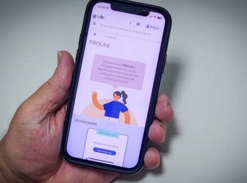 Uma mão segura um celular, cuja tela mostra o site do Prouni