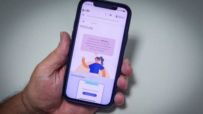 Uma mão segura um celular, cuja tela mostra o site do Prouni