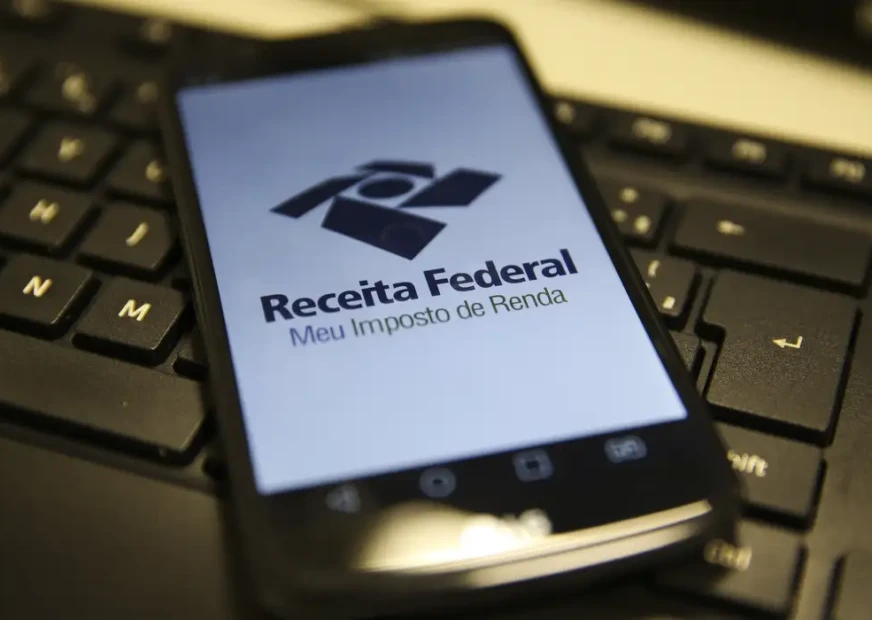 Celular com aplicativo da Receita Federal na tela sobre um teclado de computador