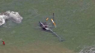 Imagem de um helicóptero tombado, de lado, dentro do mar