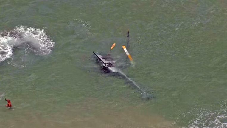 Imagem de um helicóptero tombado, de lado, dentro do mar