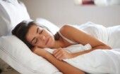 Mulher dormindo em uma cama em que tudo é branco.