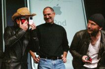 Bono Vox, vocalista do U2, brinca com aparelhos da Apple ao lado de Steve Jobs e do guitarrista The Edge.