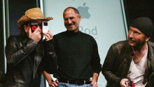 Bono Vox, vocalista do U2, brinca com aparelhos da Apple ao lado de Steve Jobs e do guitarrista The Edge.