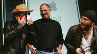Bono Vox, vocalista do U2, brinca com aparelhos da Apple ao lado de Steve Jobs e do guitarrista The Edge.