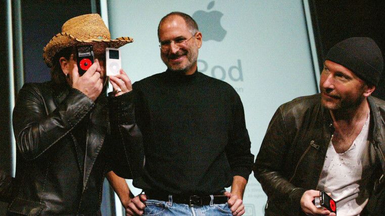 Bono Vox, vocalista do U2, brinca com aparelhos da Apple ao lado de Steve Jobs e do guitarrista The Edge.