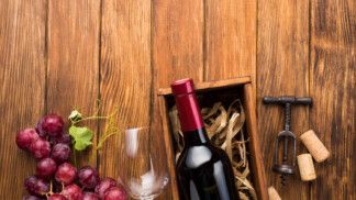 Foto mostra um vinho dentro de uma caixa com rolhas e uvas roxas ao lado