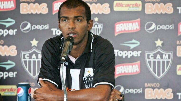 Richarlyson está sentado em frente ao microfone, com os braços cruzados