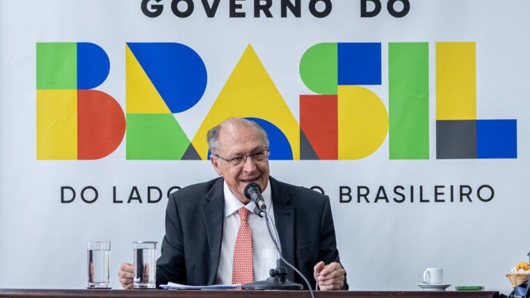 Geraldo Alckmin fala com a imprensa, à frente de um banner do governo federal