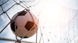 Na foto há uma bola de futebol dentro de uma rede de gol.