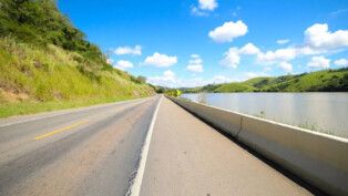 A rodovia é vista quase da altura do chão, sem carros, em dia ensolarado