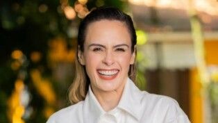 Ana Paula sorri, ela usa o cabelo para trás e uma camisa branca.