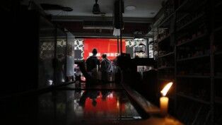 Pessoas estão no escuro, diante de uma vela acesa