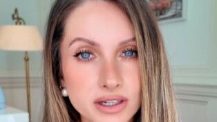 Mulher loira e de olho claro. Usa brinco de pérola.