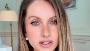 Mulher loira e de olho claro. Usa brinco de pérola.