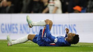 Estêvão está caído no gramado com a mão no joelho esquerdo