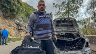 O jornalista Jamal Al-Gharabi, da Al Mayadeen, segura um colete de imprensa ao lado de um carro destruído por um ataque israelense que matou os jornalistas libaneses Fatima Ftouni, repórter da Al Mayadeen, e Mohammed Ftouni, cinegrafista, e Ali Shaib, repórter da Al Manar (Foto: Reuters)