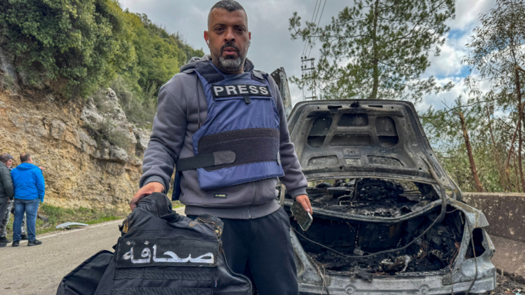 O jornalista Jamal Al-Gharabi, da Al Mayadeen, segura um colete de imprensa ao lado de um carro destruído por um ataque israelense que matou os jornalistas libaneses Fatima Ftouni, repórter da Al Mayadeen, e Mohammed Ftouni, cinegrafista, e Ali Shaib, repórter da Al Manar (Foto: Reuters)