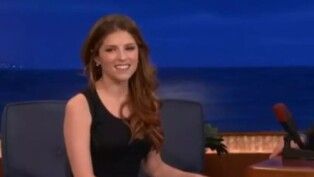 Mulher de vestido preto sentada em um sofá preto.