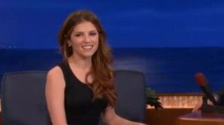 Mulher de vestido preto sentada em um sofá preto.