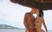 Mel Maia e seu namorado se beijam e atrás deles está uma praia.