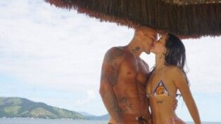 Mel Maia e seu namorado se beijam e atrás deles está uma praia.