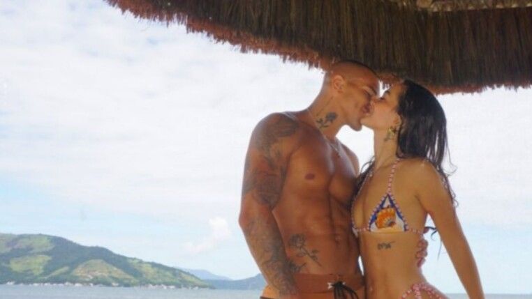 Mel Maia e seu namorado se beijam e atrás deles está uma praia.