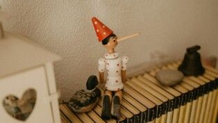Imagem de um boneco do Pinóquio, sentado sobre livros