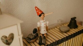 Imagem de um boneco do Pinóquio, sentado sobre livros