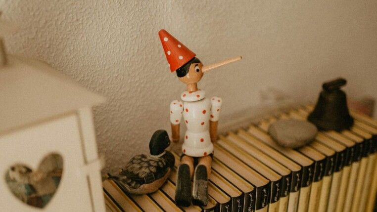 Imagem de um boneco do Pinóquio, sentado sobre livros