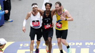 Dois corredores ajudam um terceiro na reta final da prova