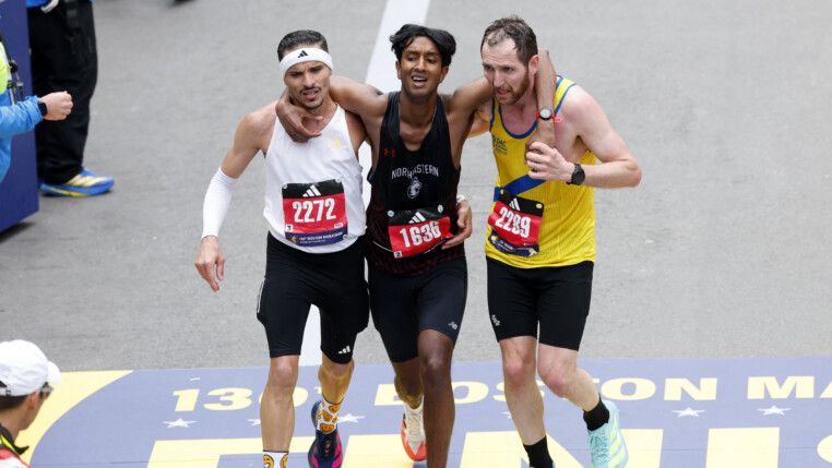Dois corredores ajudam um terceiro na reta final da prova