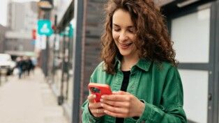 Mulher segurando celular enquanto sorri.