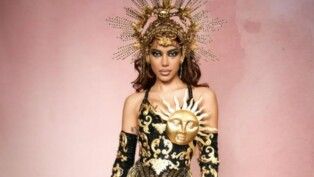 Anitta com fantasia de signo em um fundo rosa.