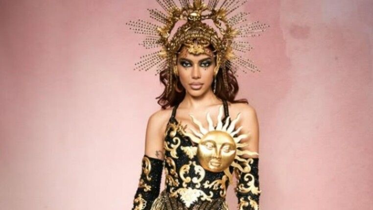 Anitta com fantasia de signo em um fundo rosa.