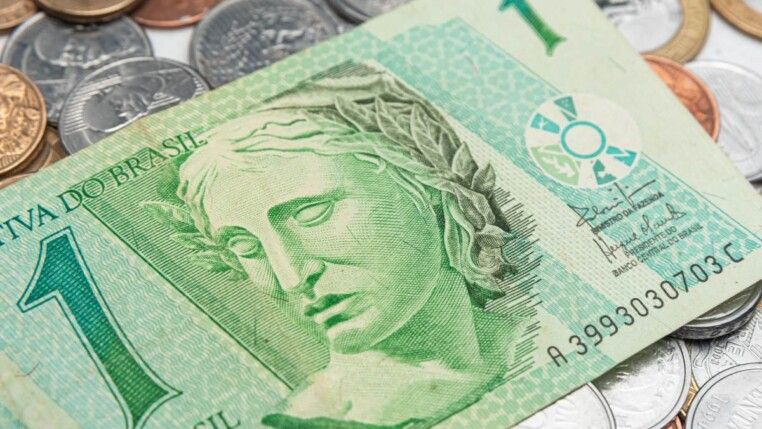 Nota de um real e diversos centavos em uma mesa.