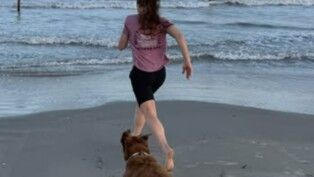 Uma mulher e um cachorrem em direção ao mar.