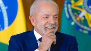 Presidente Lula sorrindo e atrás dele está a bandeira do Brasil.