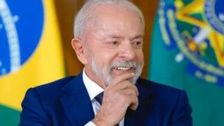 Presidente Lula sorrindo e atrás dele está a bandeira do Brasil.