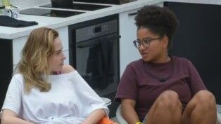 Milena e Ana Paula sentadas na cozinha olhando uma para a outra.