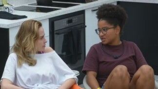 Milena e Ana Paula sentadas na cozinha olhando uma para a outra.