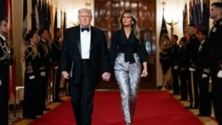 Na foto há Donald Trump do lado de sua esposa. Trump usa um smoking e Melania uma calça prata.